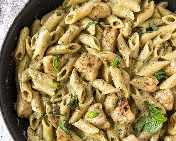 Creamy pesto chicken served with pasta garnished with basil and parmesan