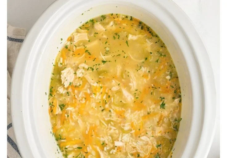 Bowl of slow cooker lemon chicken and rice soup garnished with fresh herbs.